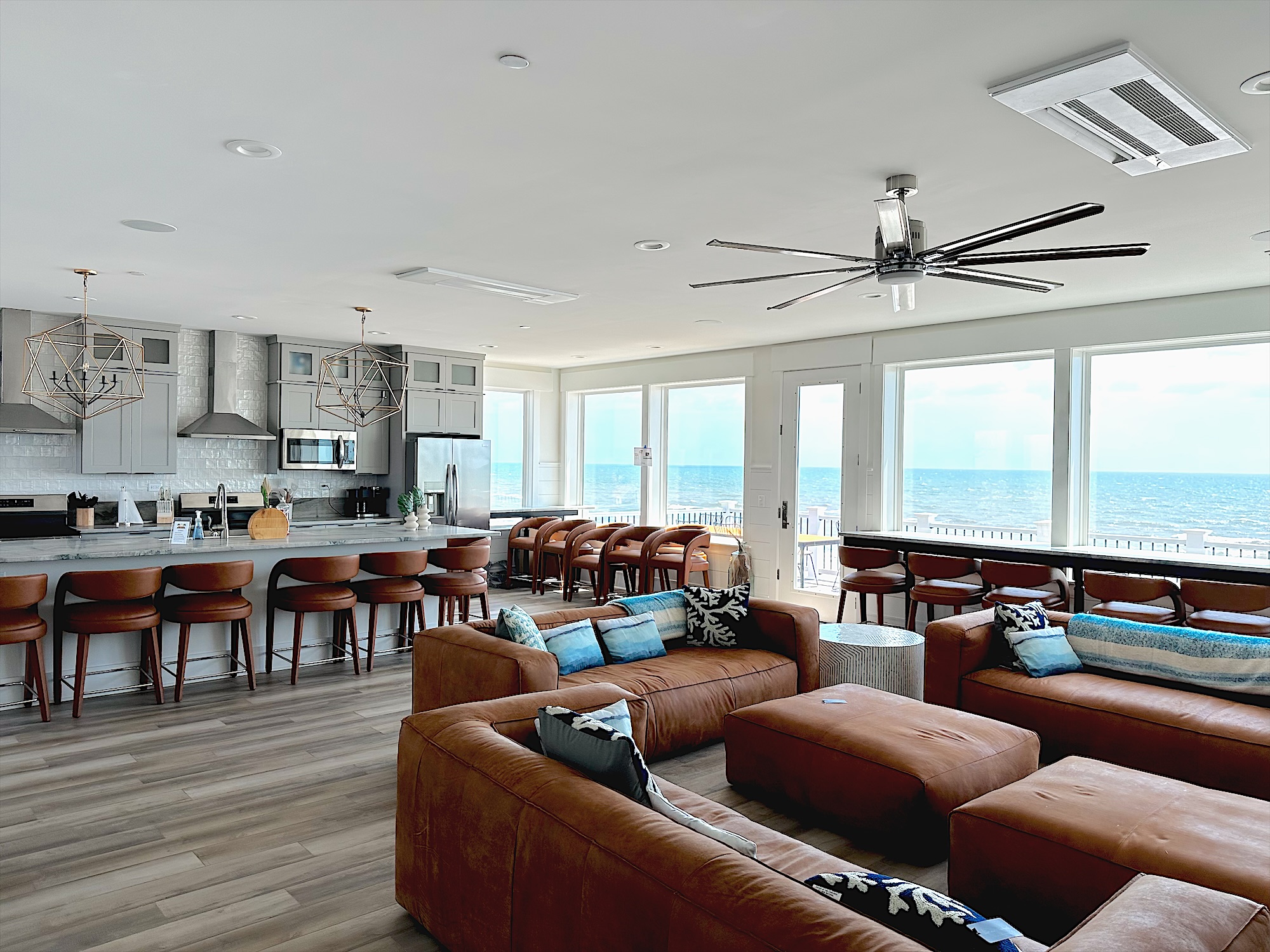 Oceanfront great room with a long stone island, gray shaker cabinetry and a wall of windows facing the ocean